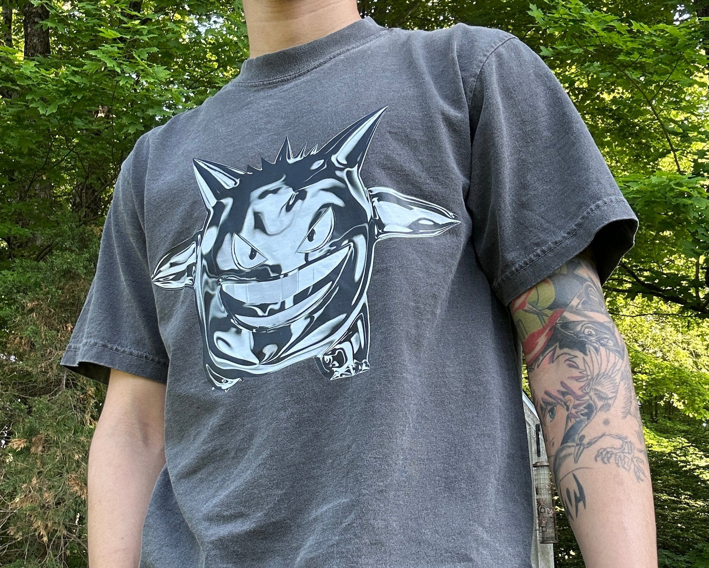 Person wearing a gray t-shirt with a chrome gengar graphic design outdoors